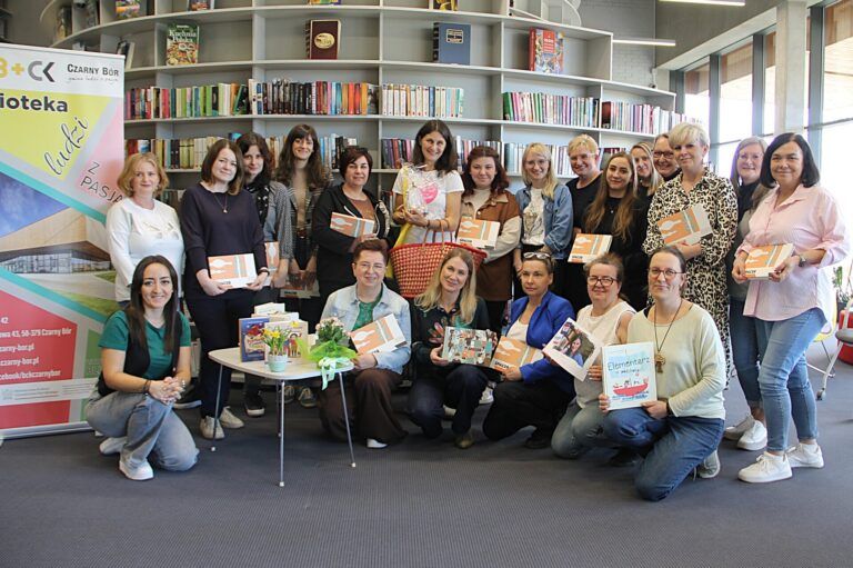 Bibliotekarze zgromadzeni w bibliotece, pozują do zdjęcia z książką w ręku