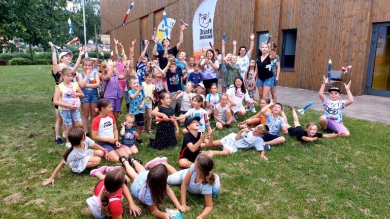 grupa dzieci przed budynkiem biblioteki trzyma w ręku zbudowane przez siebie rakiety