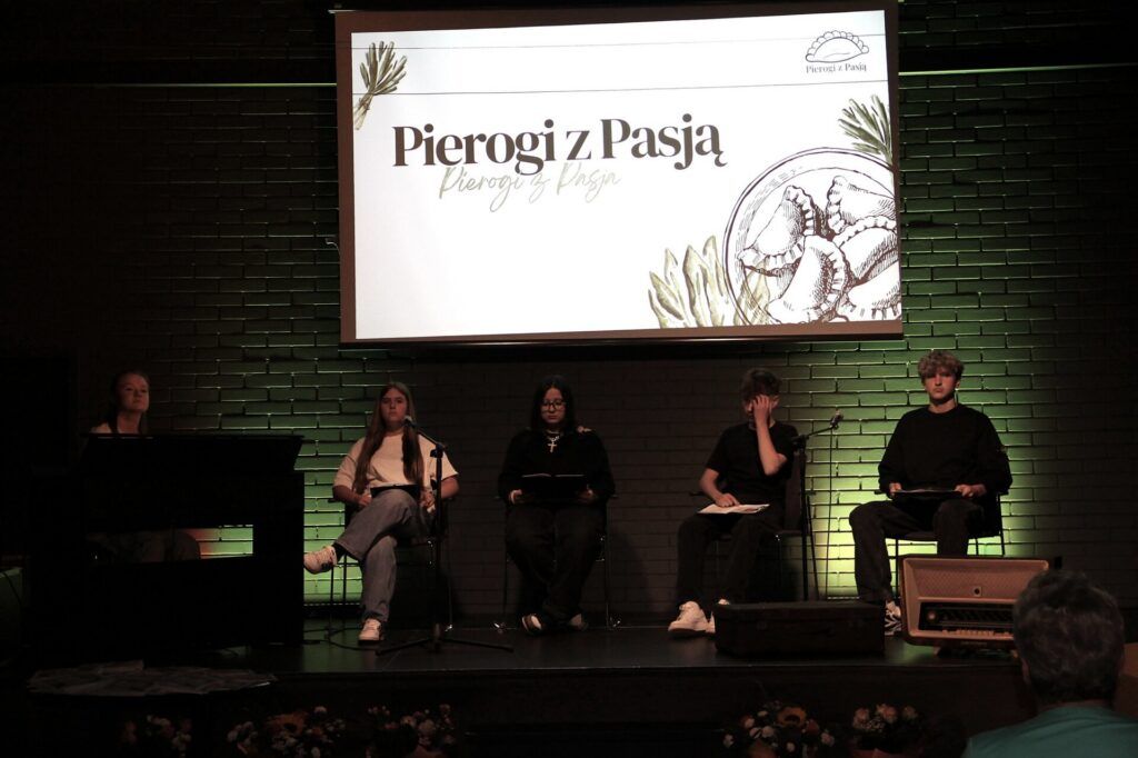 młodzi ludzie siedzą na scenie przed ekranem z napisem Pierogi z pasją