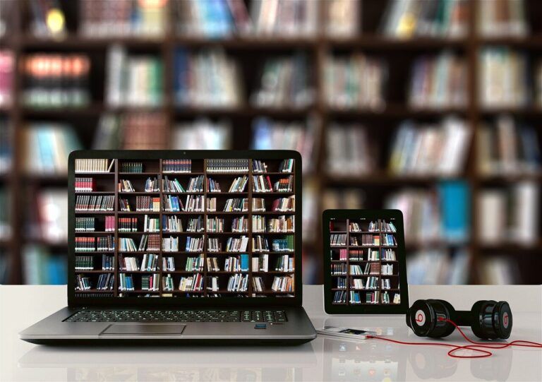 OTWARTY LAPTOP I TABLET ZE ZDJĘCIEM PÓŁEK Z KSIĄŻKAMI, W TLE REGAŁY Z KSIĄŻKAMI
