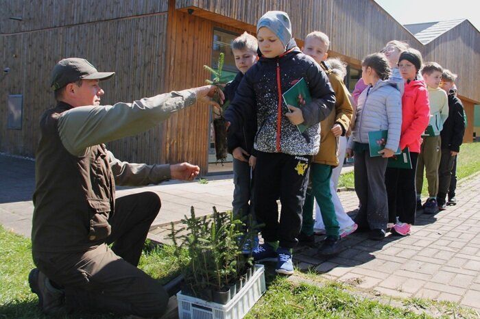 Leśniczy rozdaje sadzonki drzewek dzieciom, które uczestniczyły w spotkaniu